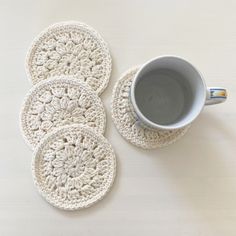 four crocheted coasters sitting next to a cup of coffee