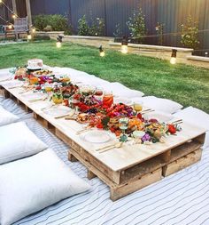 a long table is set up outside with food on it and lit candles in the background