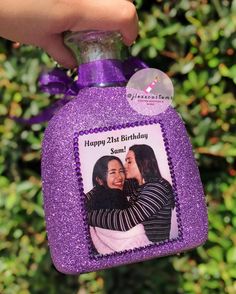 a purple bottle with a picture of two women on it is held by a hand