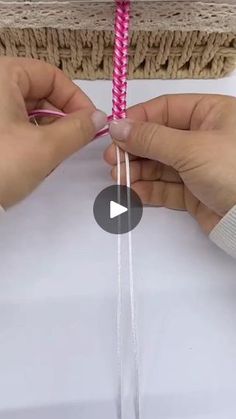 two hands holding pink and white twine on top of a piece of paper next to a basket