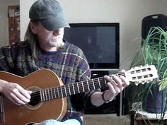 a man sitting in front of a tv holding a guitar and wearing a black hat