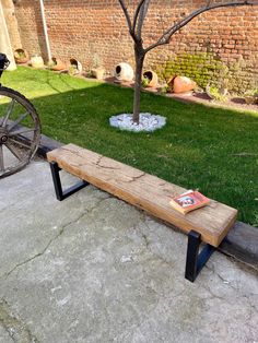 a wooden bench sitting on the side of a road next to a tree and grass