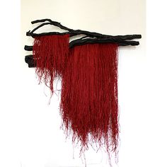 two pieces of red and black hair hanging on a white wall with sticks attached to it