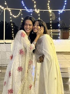 two women standing next to each other with lights in the background