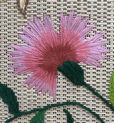 a pink flower with green leaves is on a piece of white fabric next to some thread