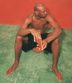 a man sitting on the floor with a basketball in his hand and an orange ball in his other hand