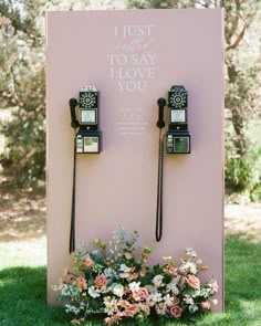 two old fashioned telephones are on display in the grass with flowers and greenery