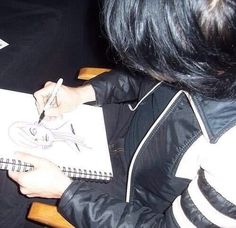 a person sitting at a table with a notebook and pen in their hand while drawing