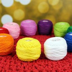 multicolored balls of yarn sitting on top of a red blanket with blurry lights in the background