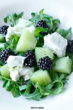 a white plate topped with cucumber, blackberries and feta on top of lettuce