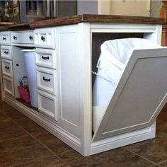 an open cabinet in the middle of a kitchen floor that is being used as a trash can