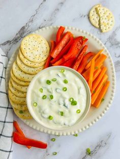 carrots and crackers on a plate with ranch dip in the middle next to them