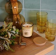 a candle and some glasses sitting on a counter next to a vase with flowers in it