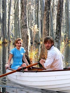 a man and woman in a boat on the water with trees behind them, both smiling