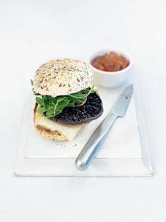 a white plate topped with a sandwich next to a bowl of sauce and a fork