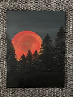 a painting with trees in the background and a red moon behind it, on a gray surface