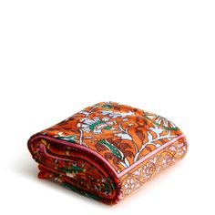 an orange and pink floral print blanket folded on top of each other in front of a white background