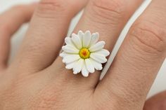 a woman's hand with a white and yellow daisy ring on top of it