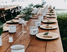 a wooden table topped with plates and cups filled with food next to plants on top of it