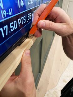 a person holding a pair of orange scissors in front of a tv screen with numbers on it