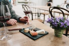 two people sitting at a table with glasses of wine and cheese on it, in front of them