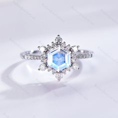 an engagement ring with a blue and white diamond center stone surrounded by small diamonds on a white background