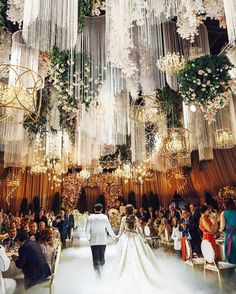 a wedding ceremony with chandeliers hanging from the ceiling and people walking down the aisle