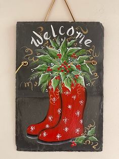 a welcome sign hanging on the wall with a red boot and holly plant in it