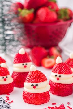 some strawberries with santa hats on them are sitting in front of a bowl of strawberries