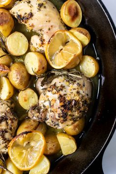 a skillet with chicken, potatoes and lemons in it on a white surface