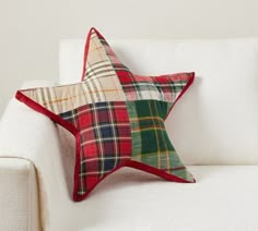 a red and green plaid star pillow sitting on a white couch next to a wall