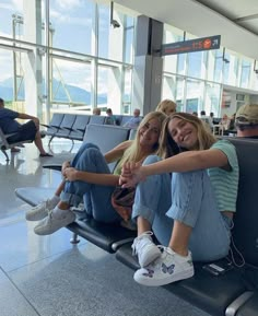 two young women sitting on the back of an airport luggage cart smiling at the camera