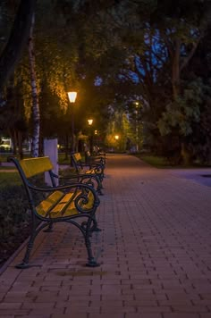 three park benches sitting next to each other on a brick walkway at night with street lights in the background