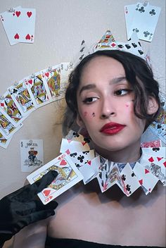 a woman wearing black gloves and red lipstick with playing cards all over her face behind her head