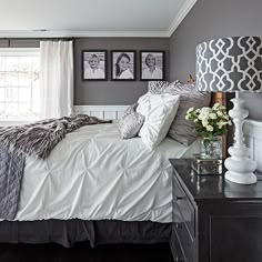 a bedroom with gray walls and white bedding, two pictures on the wall above the bed