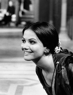 a black and white photo of a woman with her hair in a bun smiling at the camera