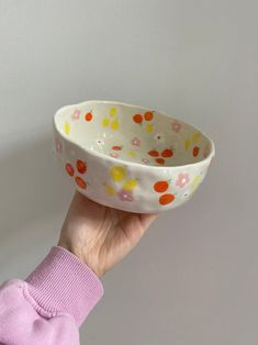 a hand holding a white bowl with multicolored polka dots