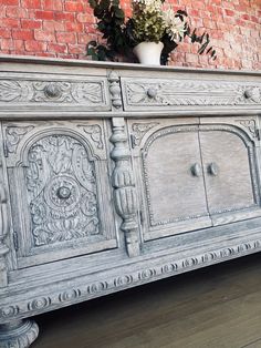 an old dresser is painted white and has flowers in it on the top shelf, next to a brick wall