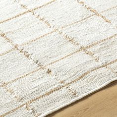 an area rug with white and beige squares on top of wooden flooring next to a wood table