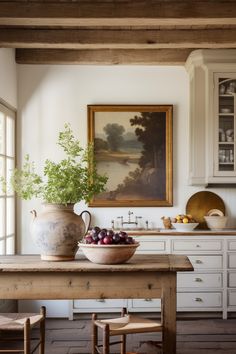 a bowl of fruit sits on a table in the middle of a room with white cabinets