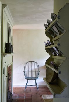 a chair sitting next to a shelf filled with plates and pans on top of it