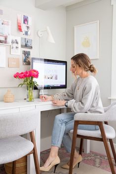 a woman sitting at a desk with a computer and flowers in front of the monitor