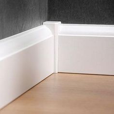 the corner of a room with a wooden floor and black wall behind it, in front of a white door