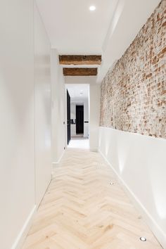 an empty hallway with white walls and wood flooring on the other side is a brick wall