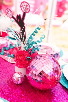 a table topped with pink and blue plates covered in disco ball centerpieces next to a vase filled with flowers