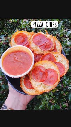 a person holding a plate of pizza chips with pepperoni and tomato sauce on them