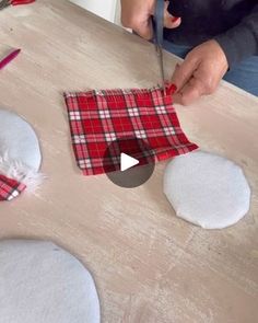 a person cutting fabric with scissors on top of a wooden table next to snowballs