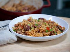 a white bowl filled with rice and meat on top of a wooden table next to a red casserole dish