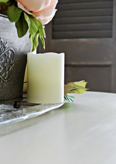 a white candle sitting on top of a table next to a vase with pink flowers