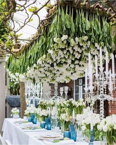 a table topped with lots of white flowers and tall vases filled with green plants